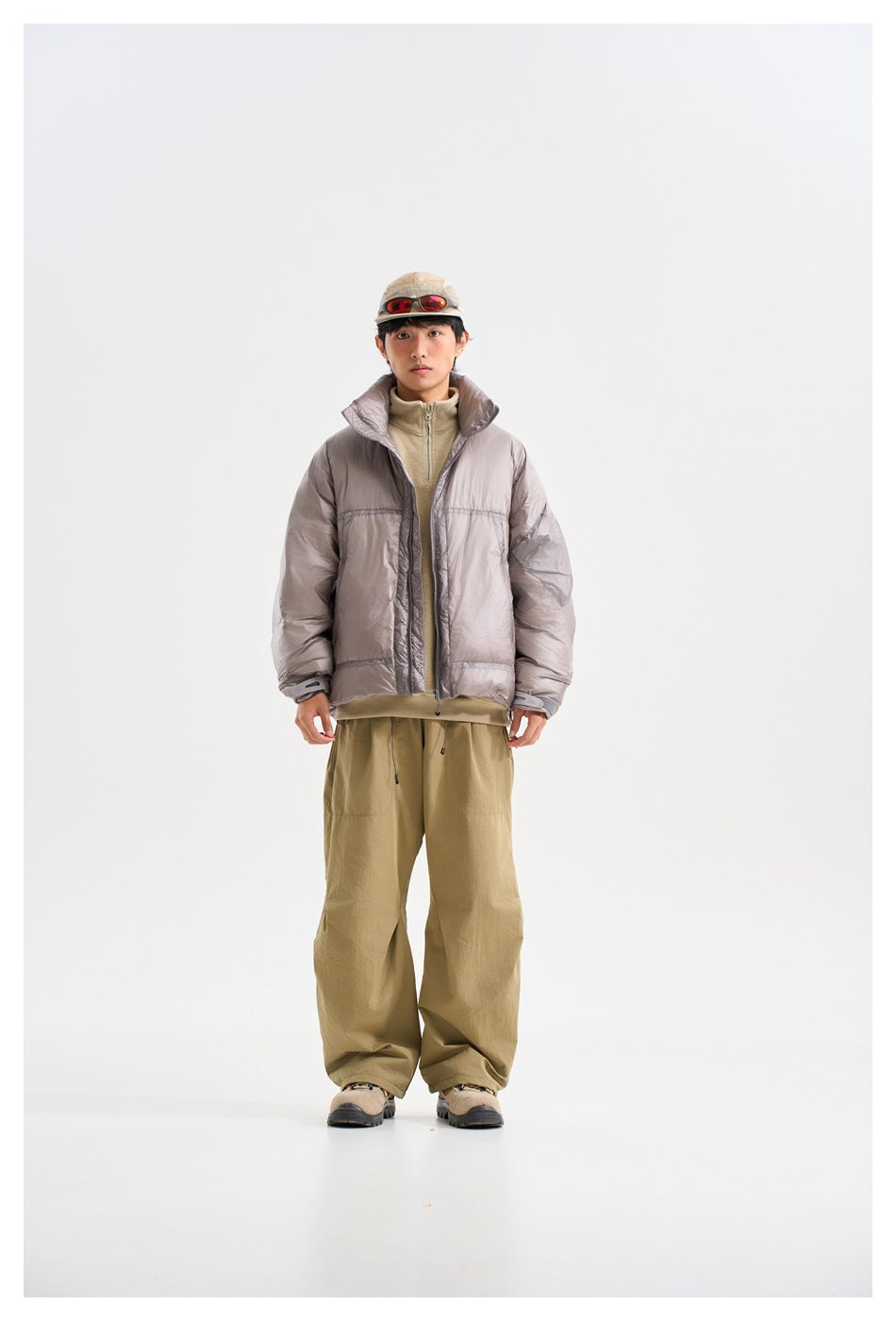 Model wearing a gray puffer jacket open over a tan top with khaki wide-leg pants, cap and boots