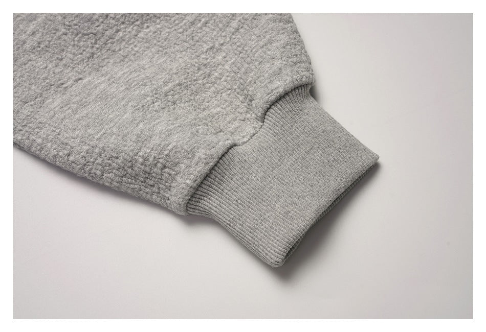 Close-up of a gray textured sweatshirt sleeve ending in a ribbed cuff.
