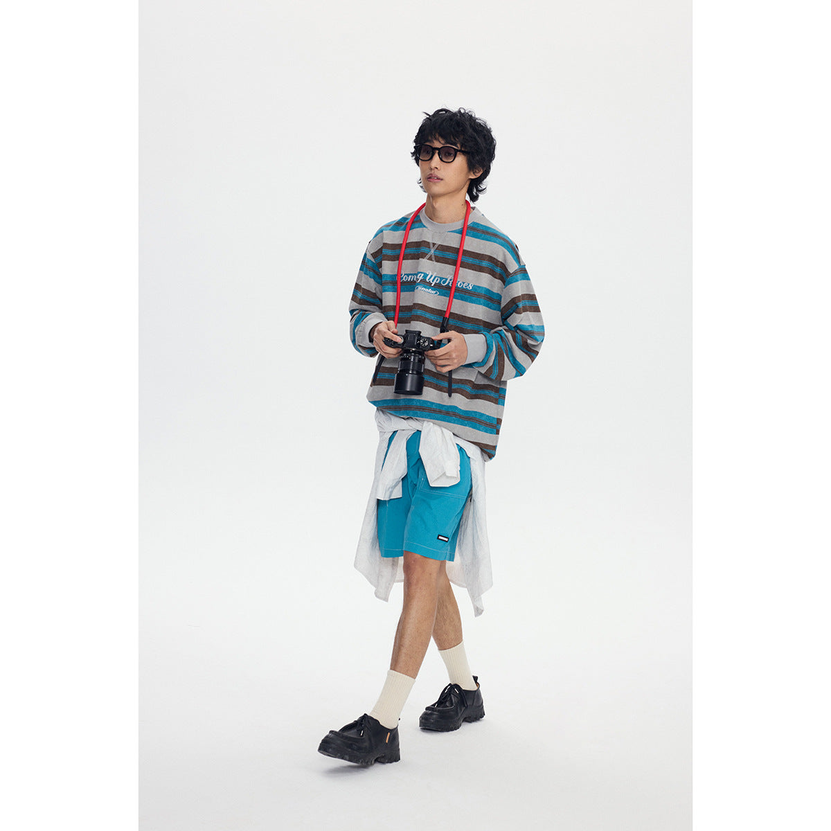 Model wearing an oversized gray sweatshirt with teal and brown stripes, bright teal shorts, and a white shirt tied at the