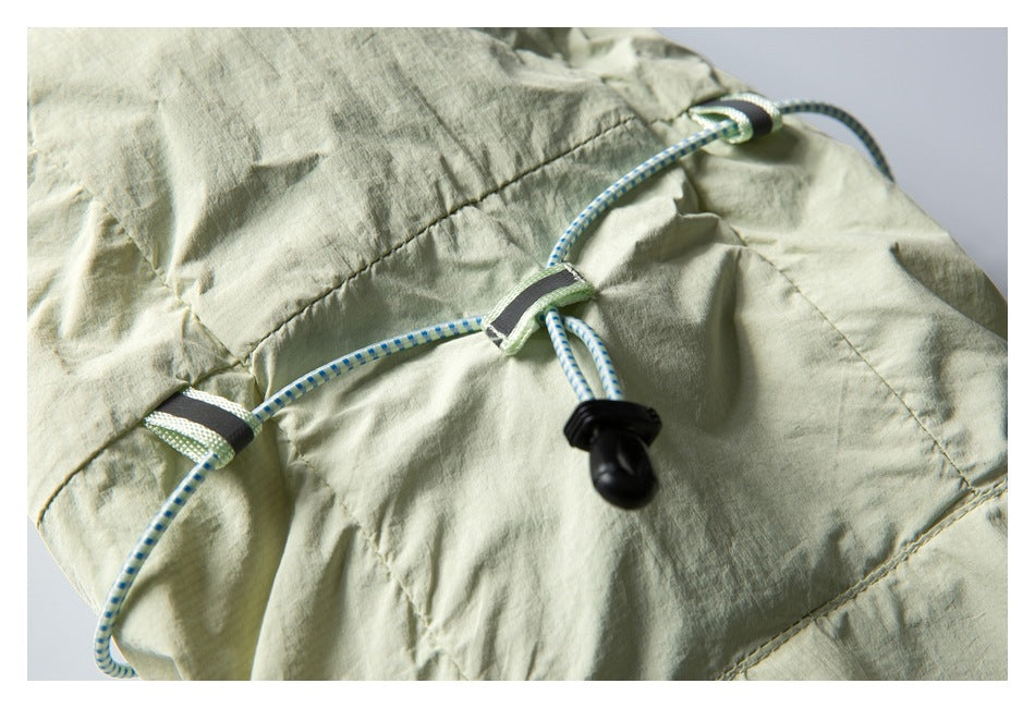 Pale sage garment detail with a blue-and-white adjustable drawcord, fabric loops, and black toggle.