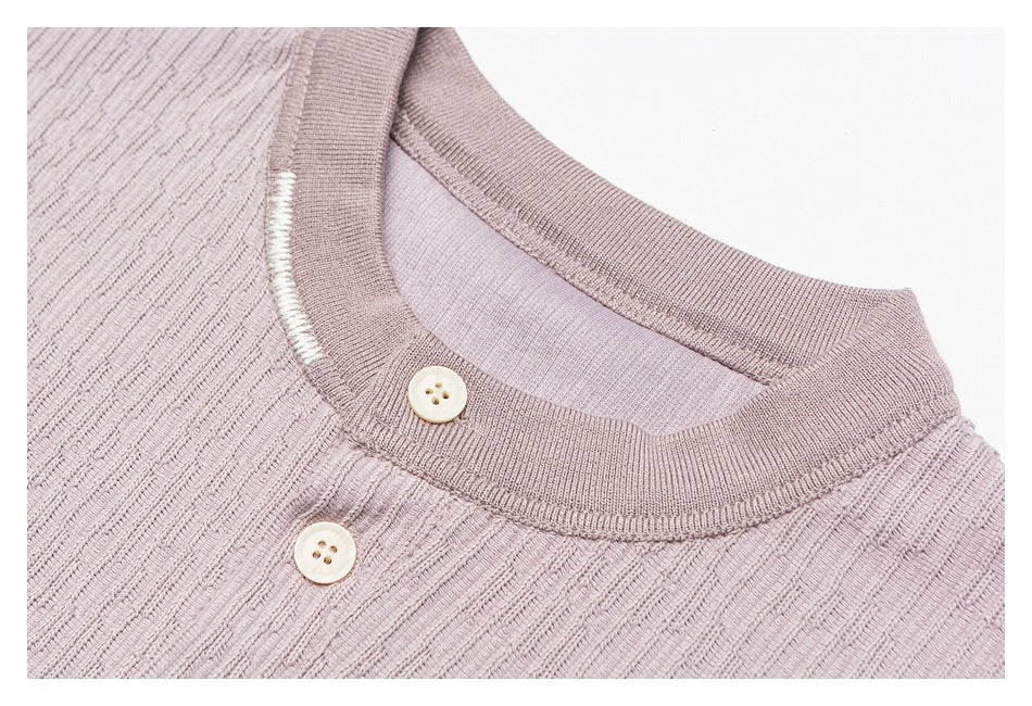 Close-up of a mauve knit top's ribbed round neckline, white contrast stitching, and two cream buttons.