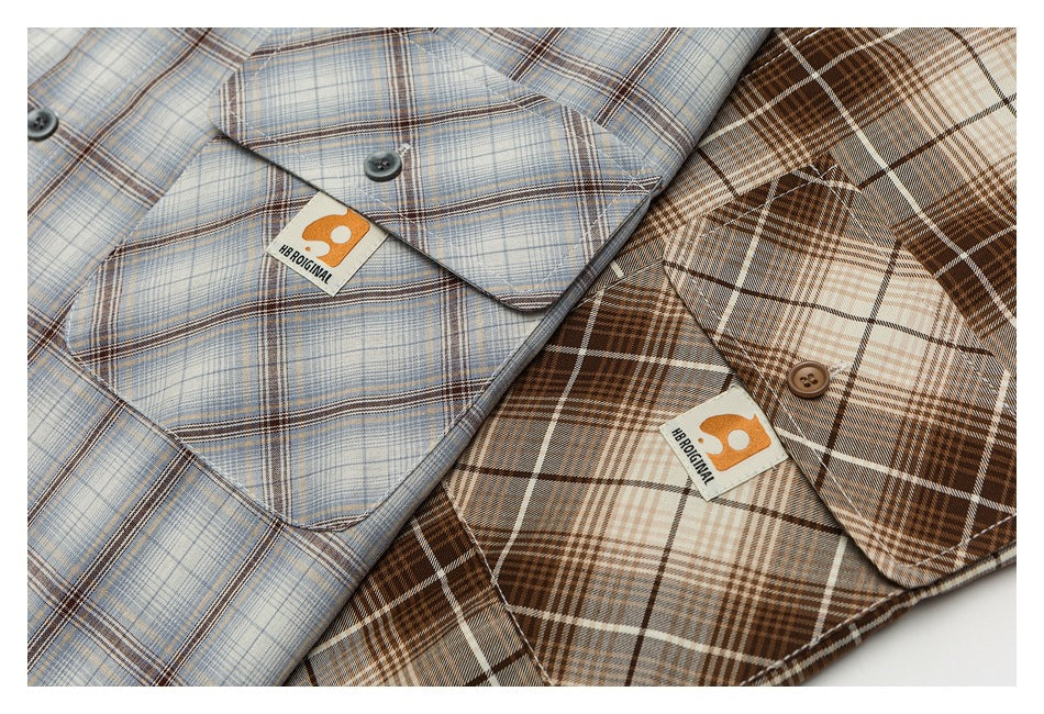 Close-up of two plaid shirt pockets in blue-gray and brown, each with a button and sewn label.