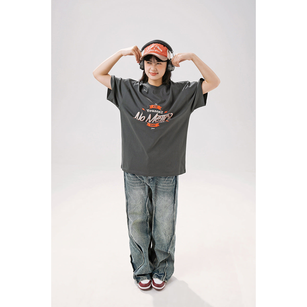 Model wearing a charcoal gray oversized graphic T-shirt, shown from the front with arms raised.