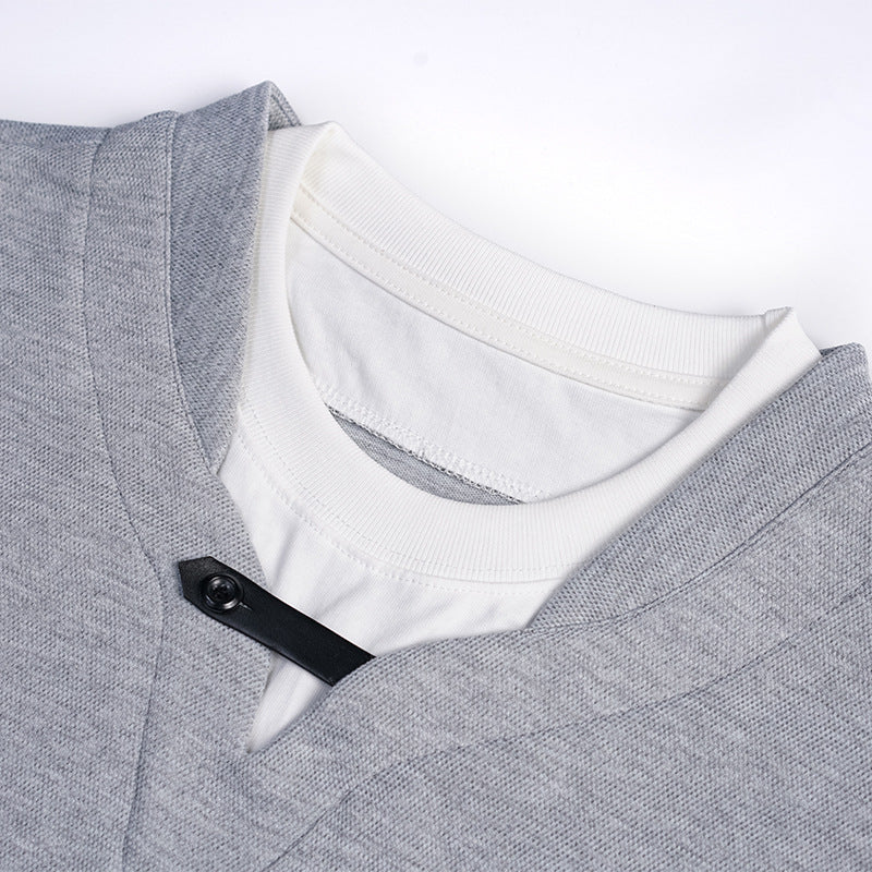 Close-up of a heather gray V-neck shirt layered over a white crewneck, with a black buttoned tab at the neckline.