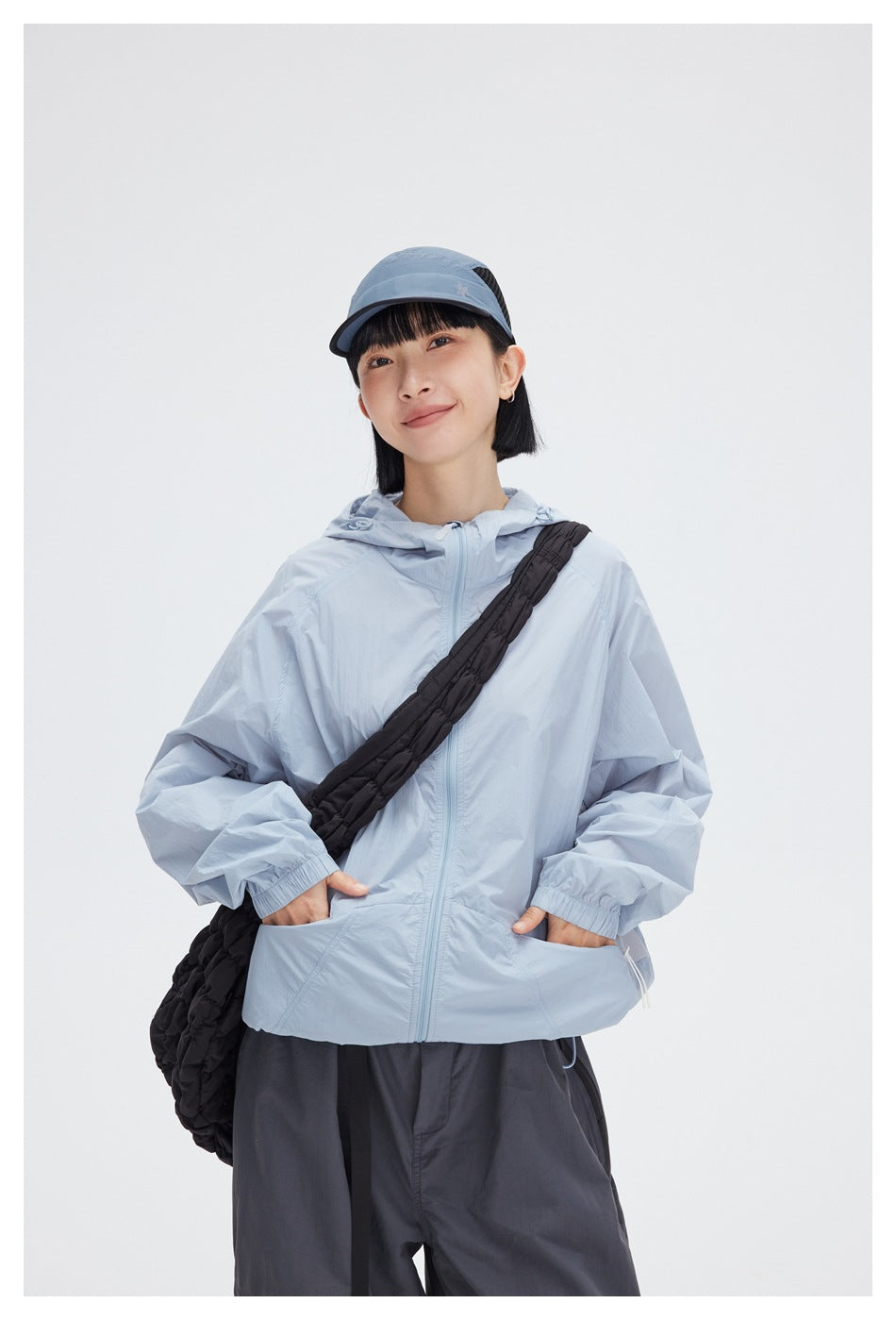 Model wearing a pale blue zip-front hooded jacket with elastic cuffs and front pockets, paired with dark pants.
