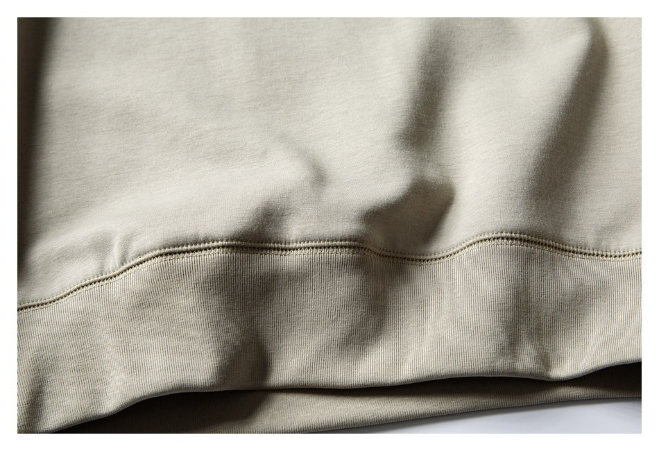 Close-up of the light beige sweatshirt's ribbed bottom hem and stitched seam.