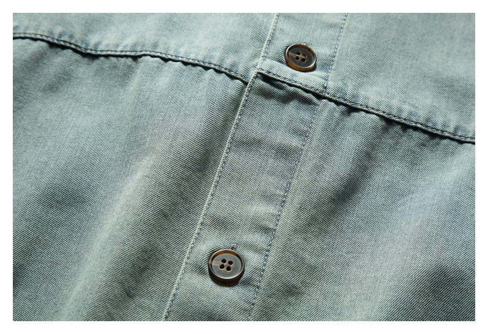 Close-up of two dark buttons and the stitched placket on light blue denim.