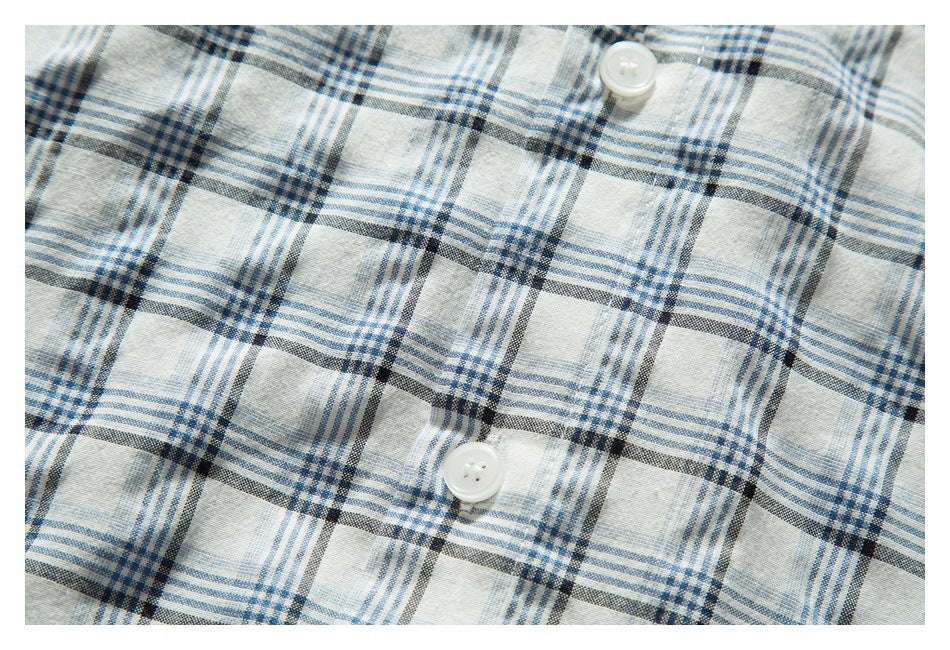 Close-up of two white buttons on a white shirt with a blue and charcoal plaid pattern.