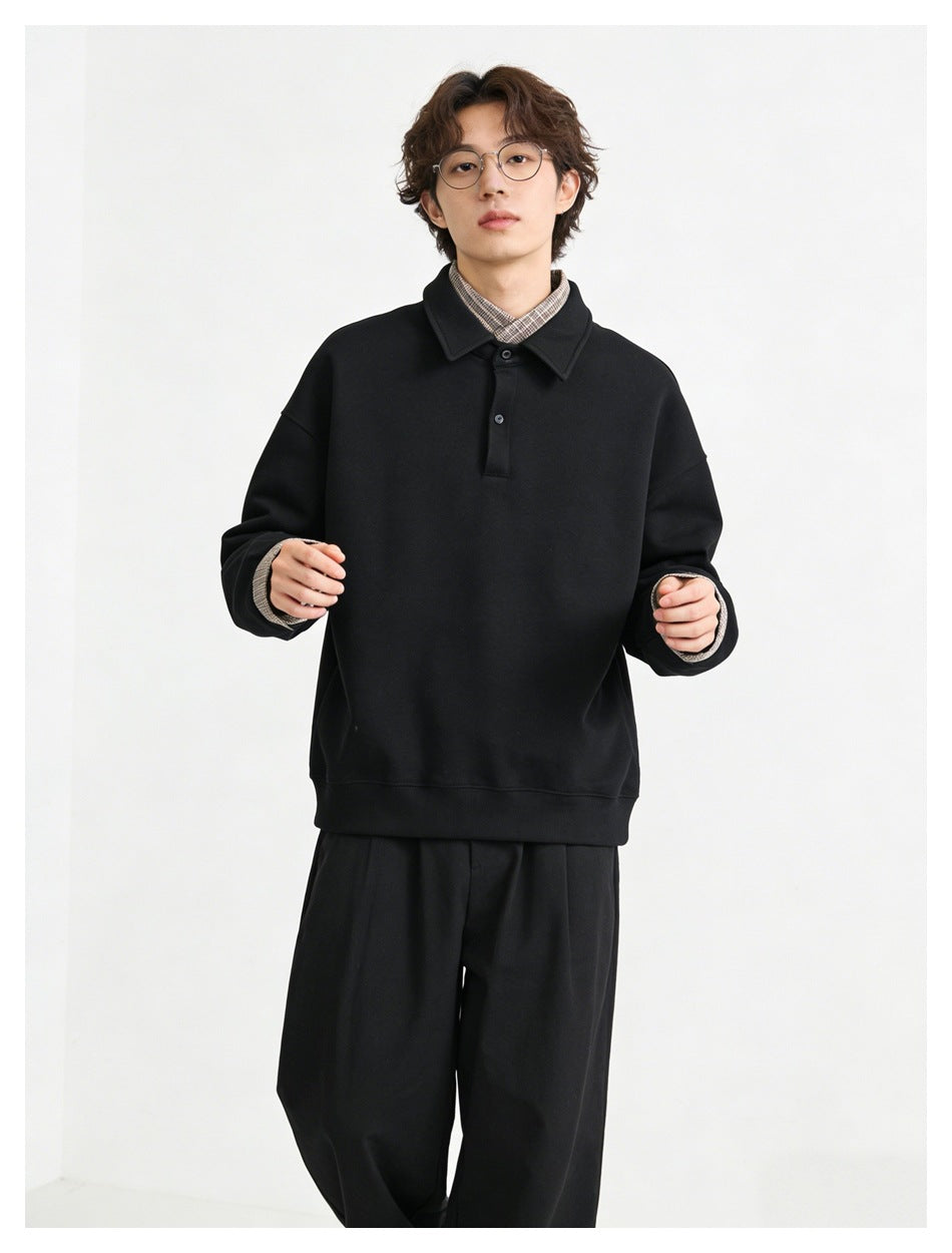 Model wearing a black collared pullover with a short button placket and checked shirt cuffs and collar.