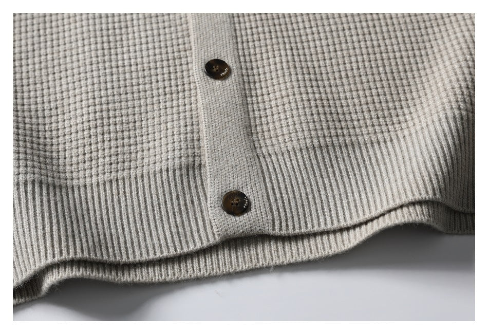 Close-up of a light gray textured knit cardigan front, showing two dark buttons and a ribbed hem.