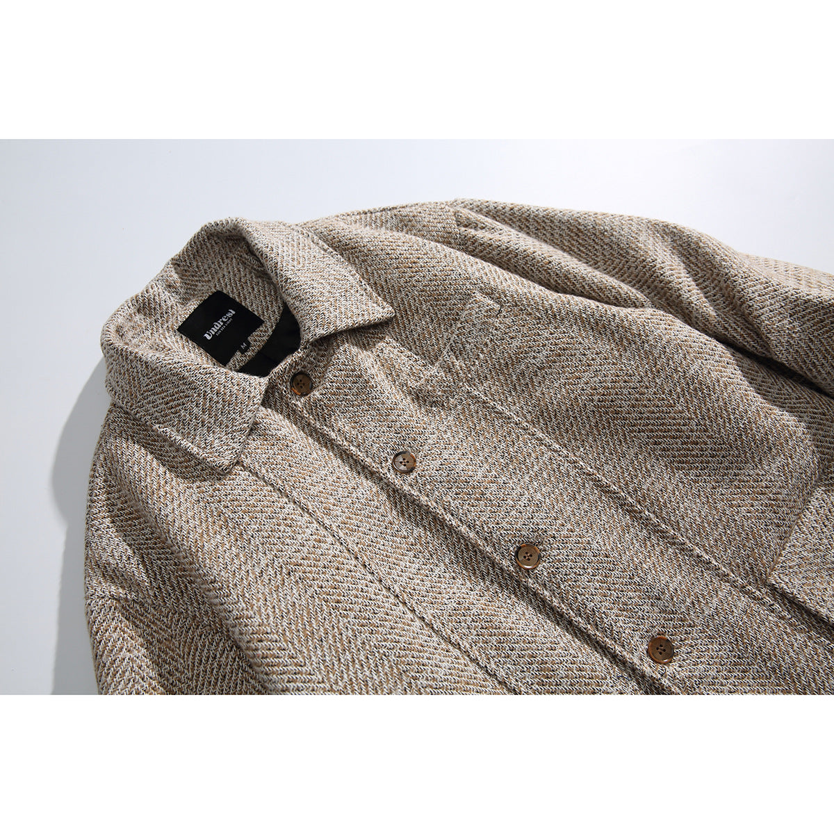 Close view of a beige patterned coat collar, brown buttons, and a black neck label.
