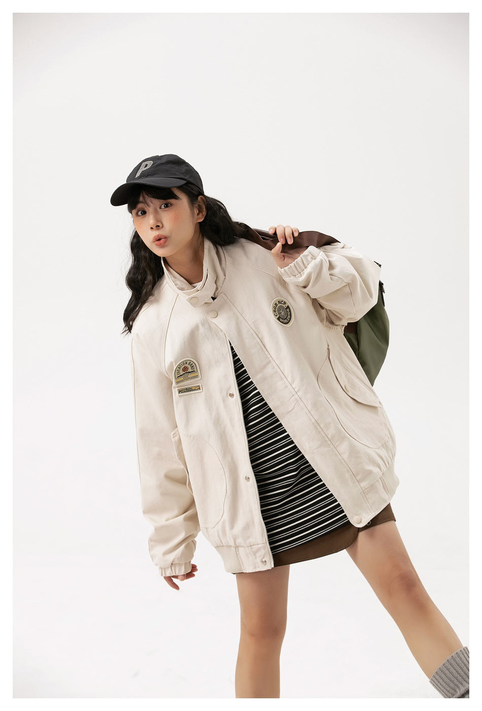 Model wearing an oversized cream jacket with decorative patches, large pockets and elastic cuffs, shown from the front.
