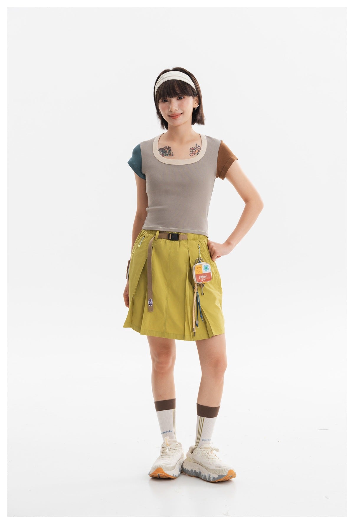 Model wearing a taupe fitted top with contrasting teal and brown sleeves and a yellow-green skirt.