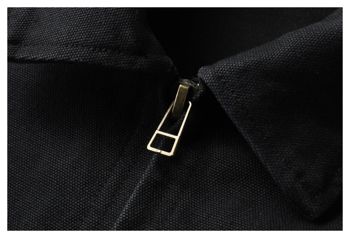 Close-up of a brass-tone zipper pull between the pointed collar edges of a black jacket.