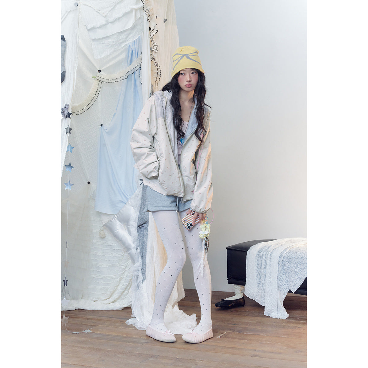 Model wearing an off-white tiny-print hooded zip jacket, gray shorts, dotted white tights, and a yellow beanie.