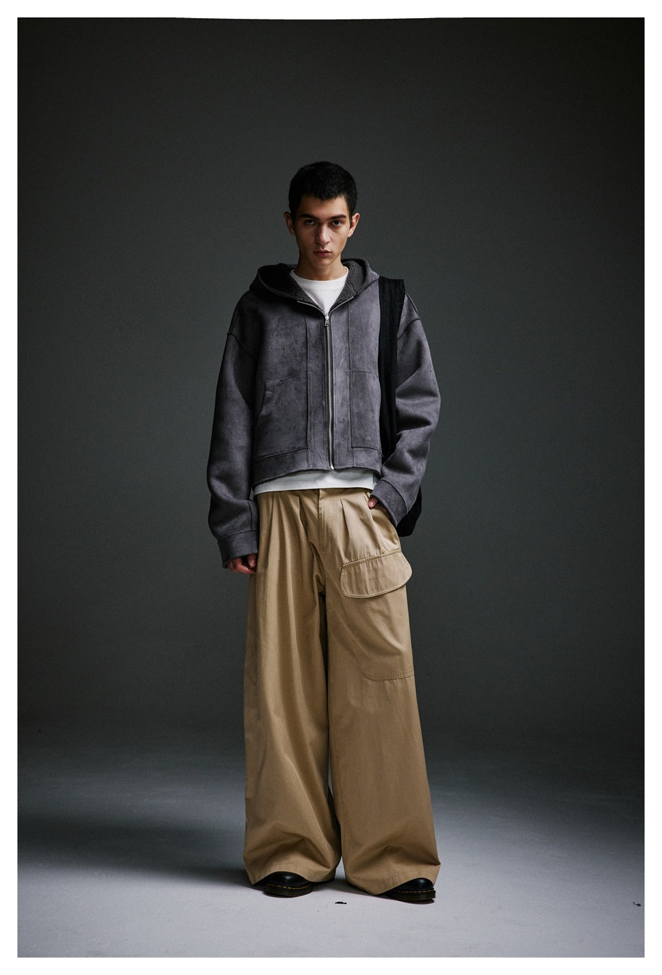 Model wearing khaki wide-leg pleated pants with a flap pocket, a gray hooded zip jacket and black shoes, front view