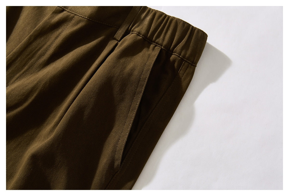 Close-up of olive-brown trousers showing the gathered waistband, belt loop, and side pocket seam.