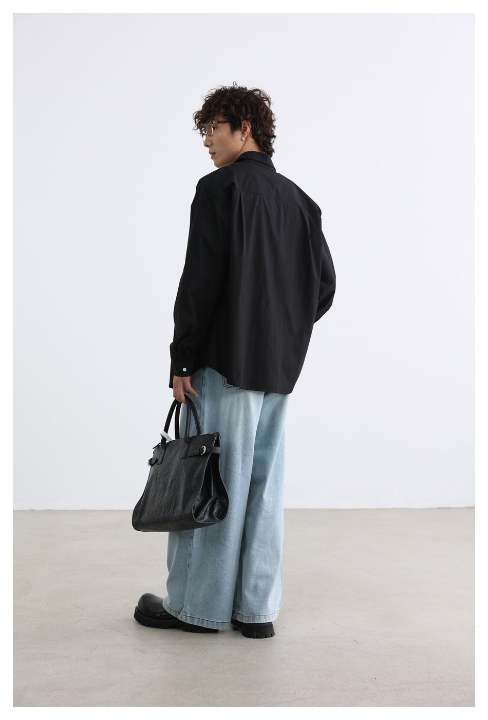 Rear view of a model in a black button-up shirt and light blue wide-leg jeans.