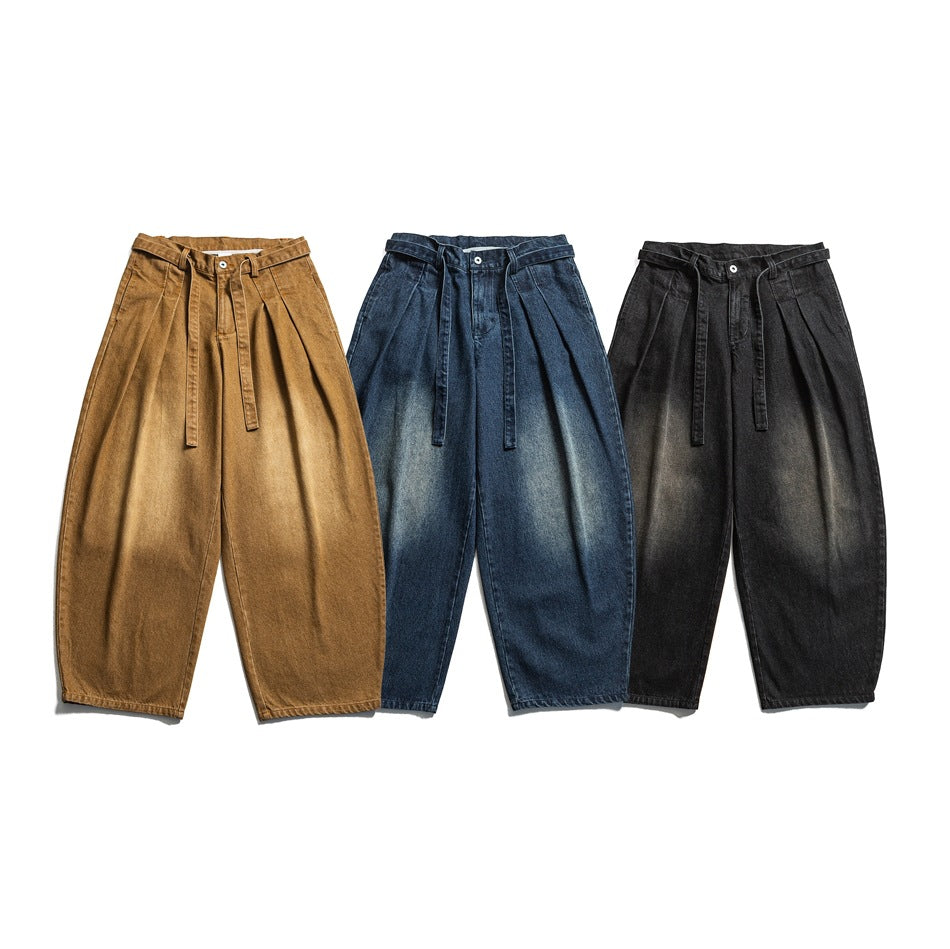 Three pairs of pleated, tapered trousers shown from the front in ochre, blue denim, and black.