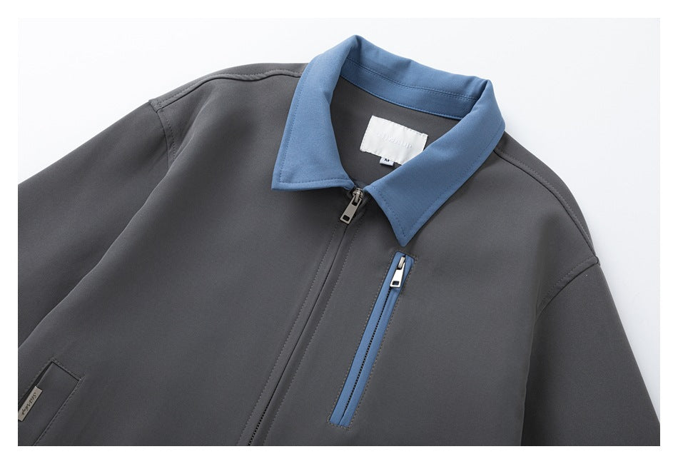Close-up of a charcoal-gray jacket showing its blue collar, front zipper, and blue-trimmed vertical zip pocket.