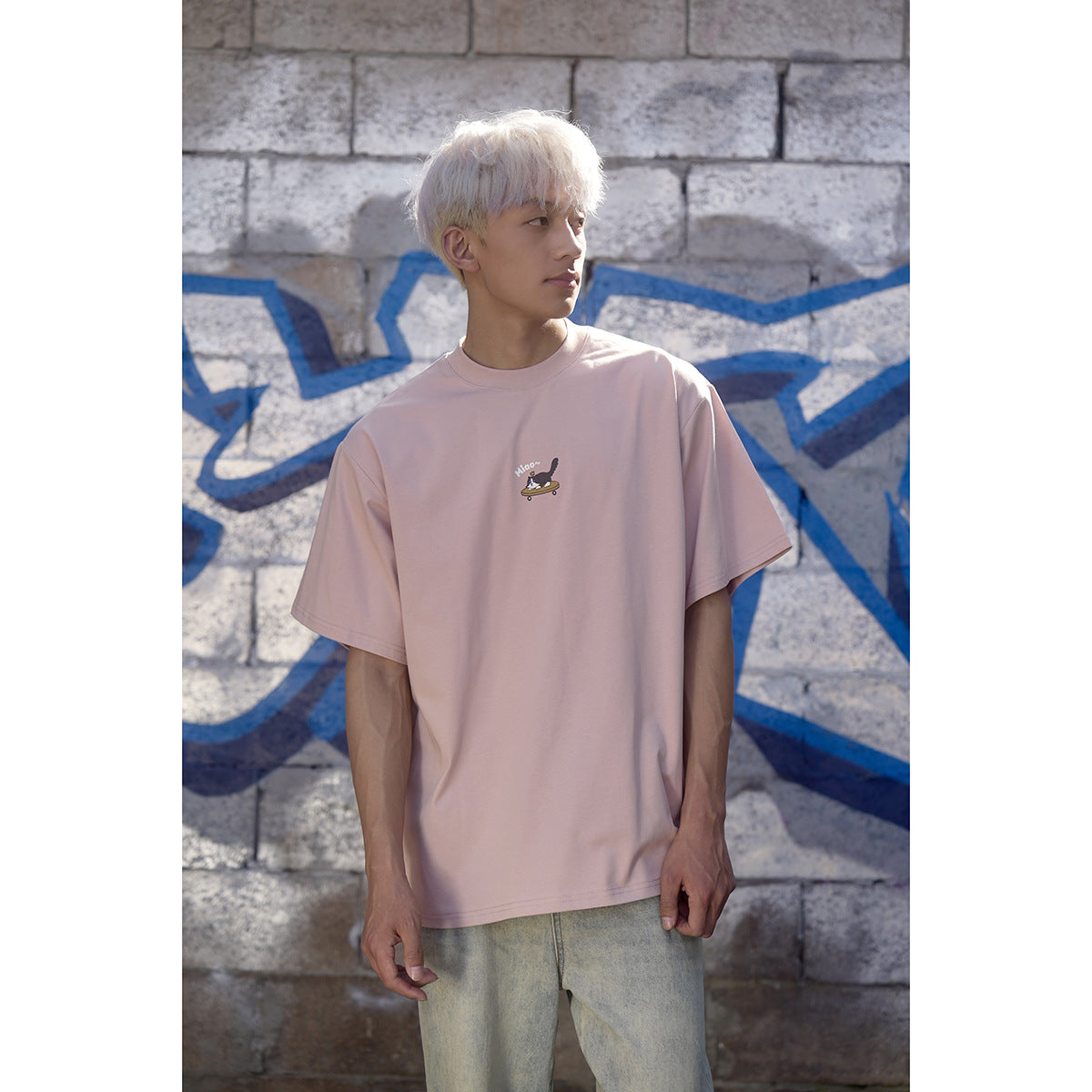 Model wearing an oversized pale pink crew-neck T-shirt with a small illustrated chest graphic.