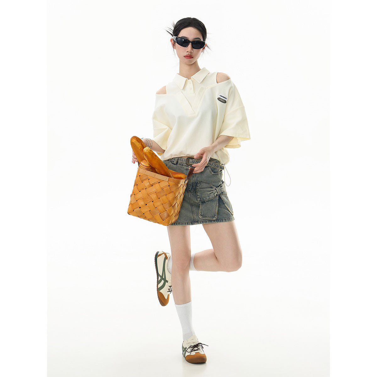 Model wearing an ivory cutout-shoulder polo and a gray denim mini skirt, holding a woven basket.