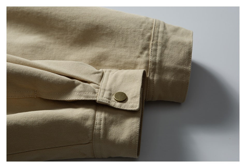 Close-up of a beige jacket sleeve cuff with a brass-colored snap tab.