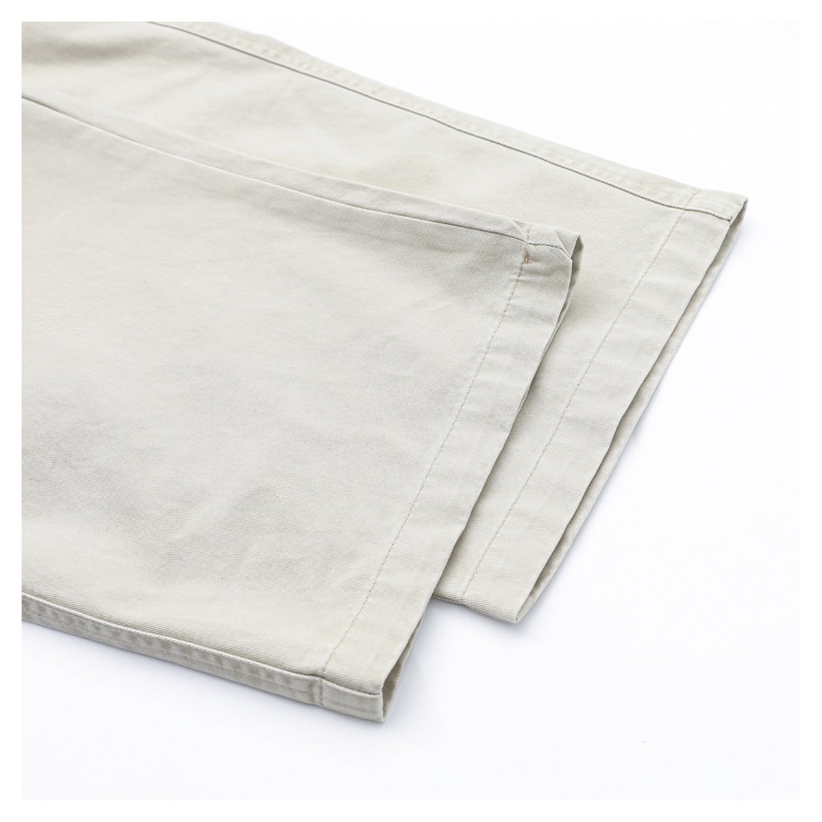 Close-up of the straight hems and stitched seams on light beige trousers.