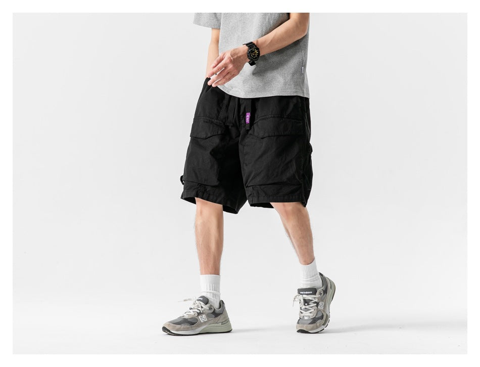 Angled front view of a model wearing black cargo shorts with large flap pockets.