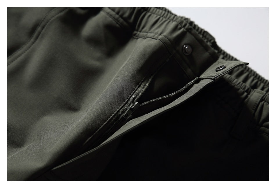 Close-up of dark olive pants showing an elastic waistband and zip fly.