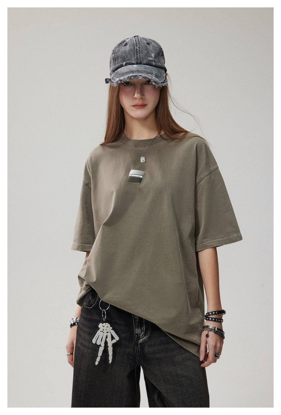 Woman wearing an olive green oversized T-shirt with a small chest graphic, a washed denim cap and dark jeans