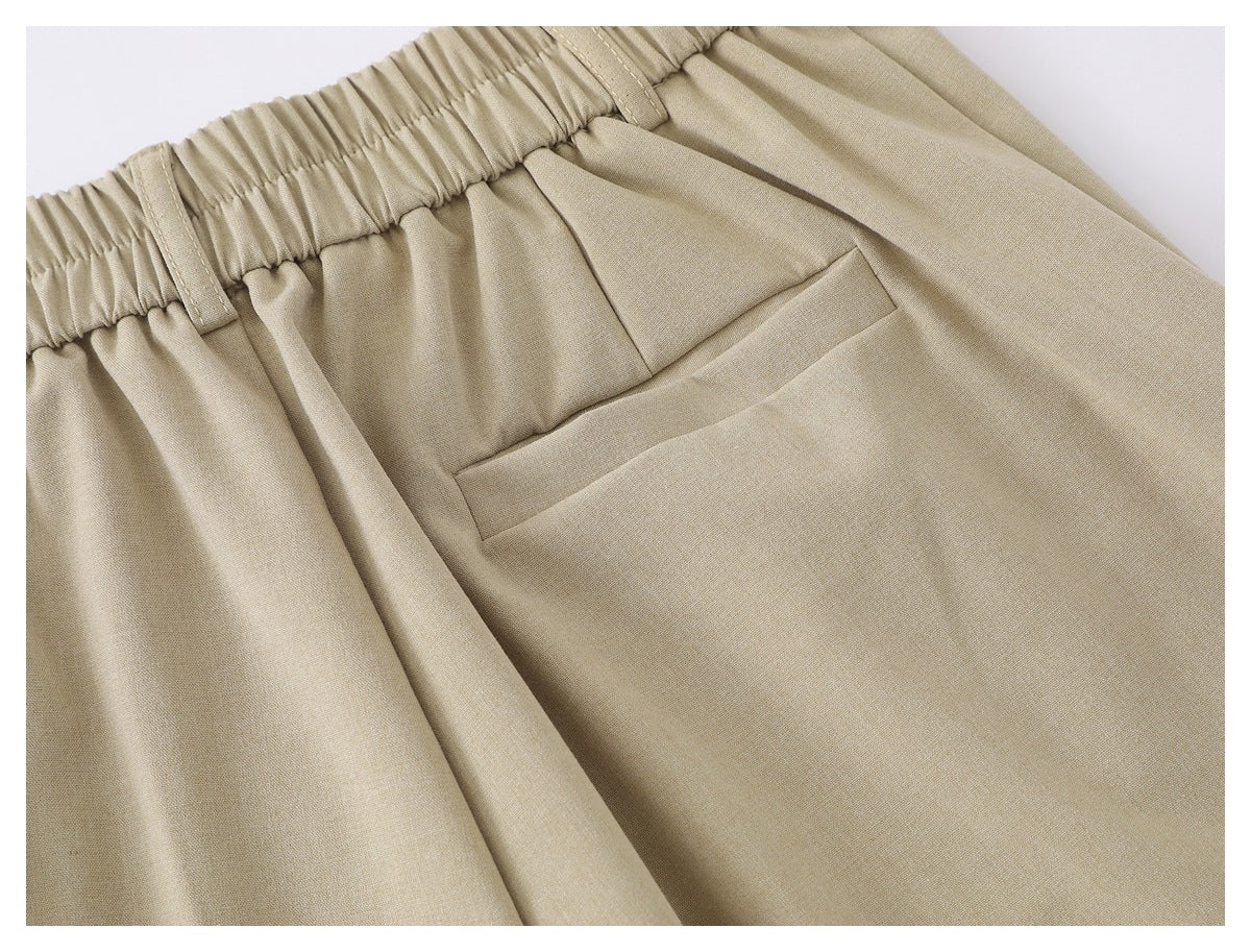 Close-up of beige trousers showing a welt back pocket, gathered waistband, and belt loops.