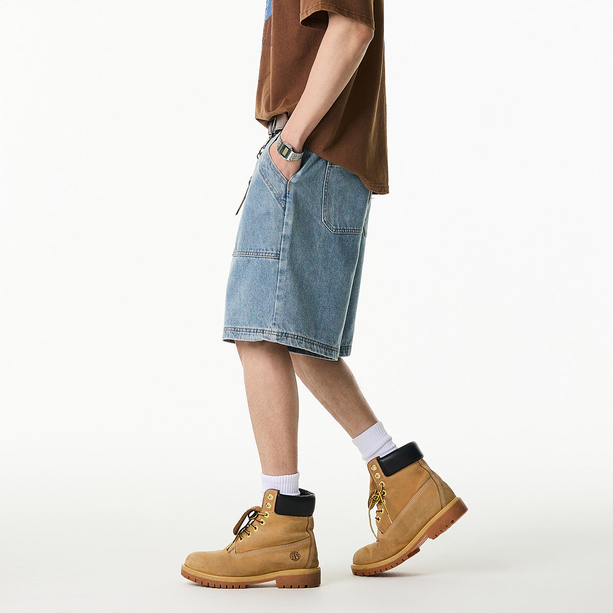 Side view of a person wearing loose light-wash denim shorts with a brown T-shirt and tan lace-up boots.