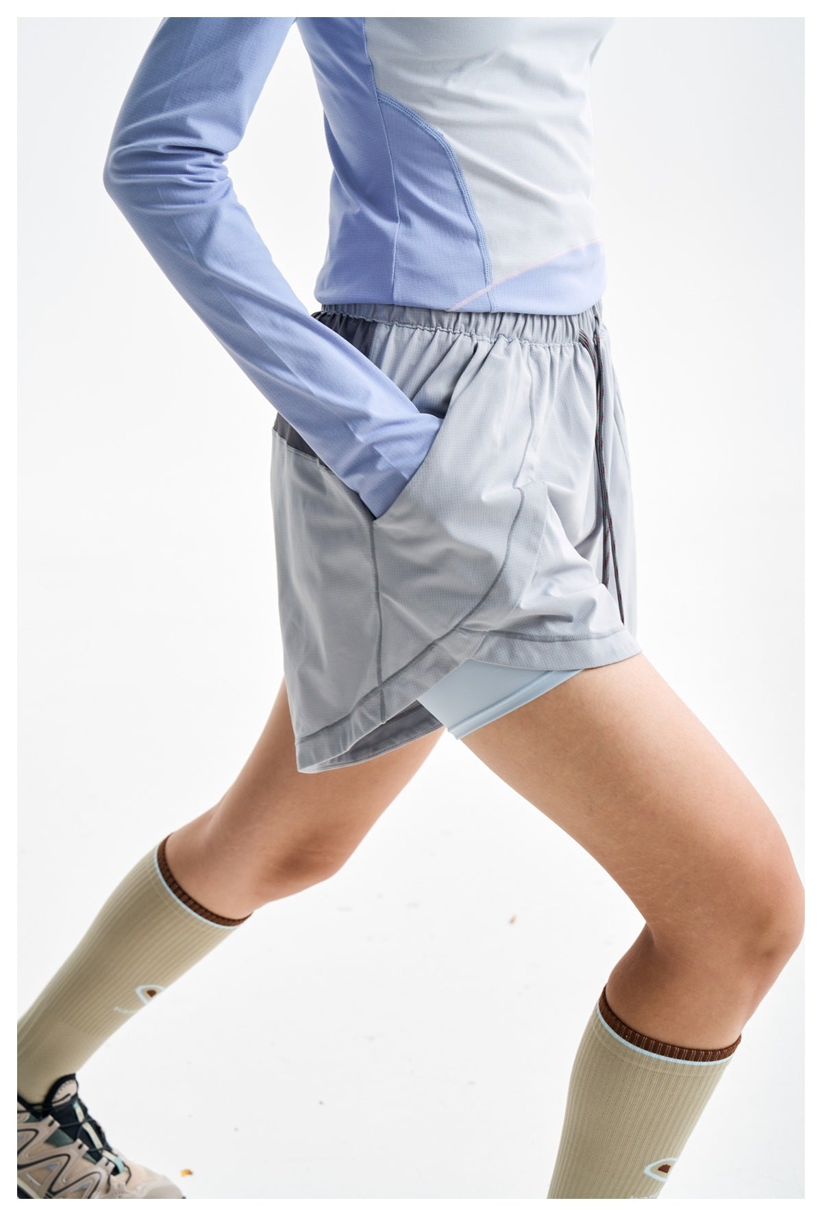 Close-up of gray running shorts on a model, showing the elastic waist, side pocket, curved hem and inner shorts.