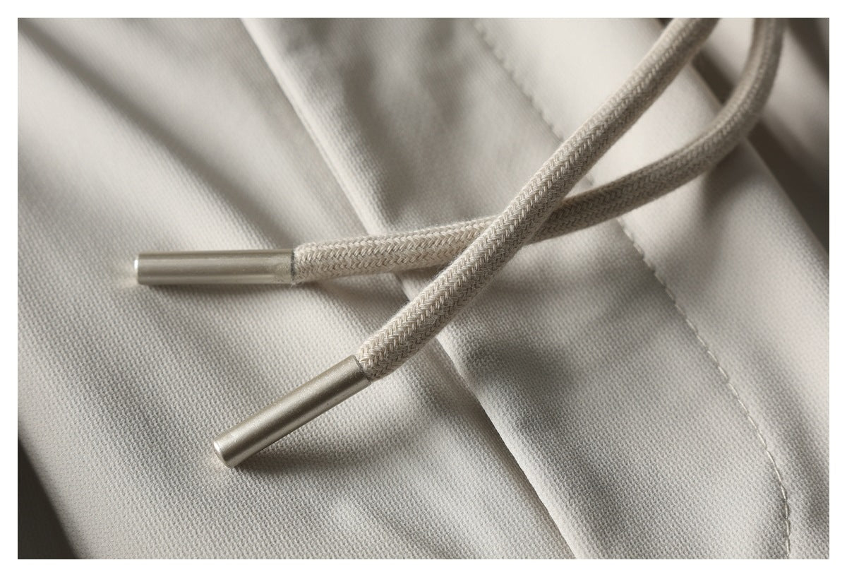 Close-up of braided drawstrings with metal tips against light beige pants fabric.