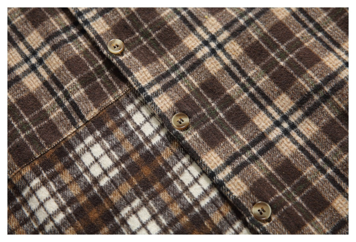Close-up of a brown, tan, cream and black plaid shirt front with buttons and a chest pocket.