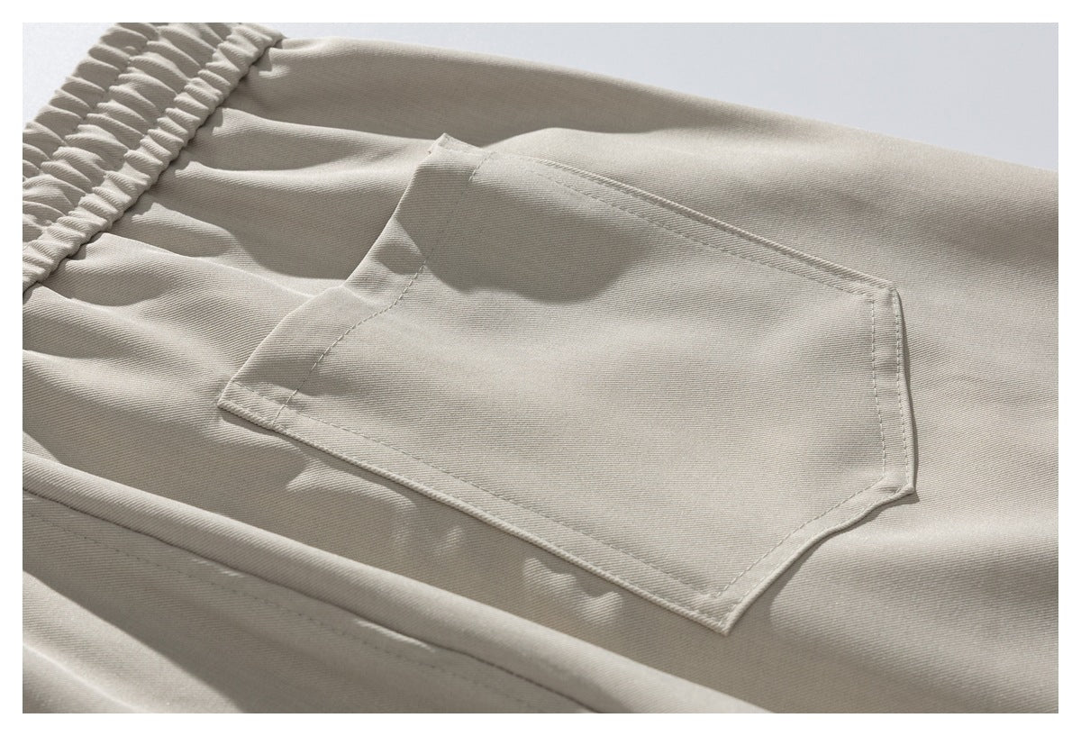 Close-up of a large rectangular patch pocket on beige trousers beside the elastic waistband.