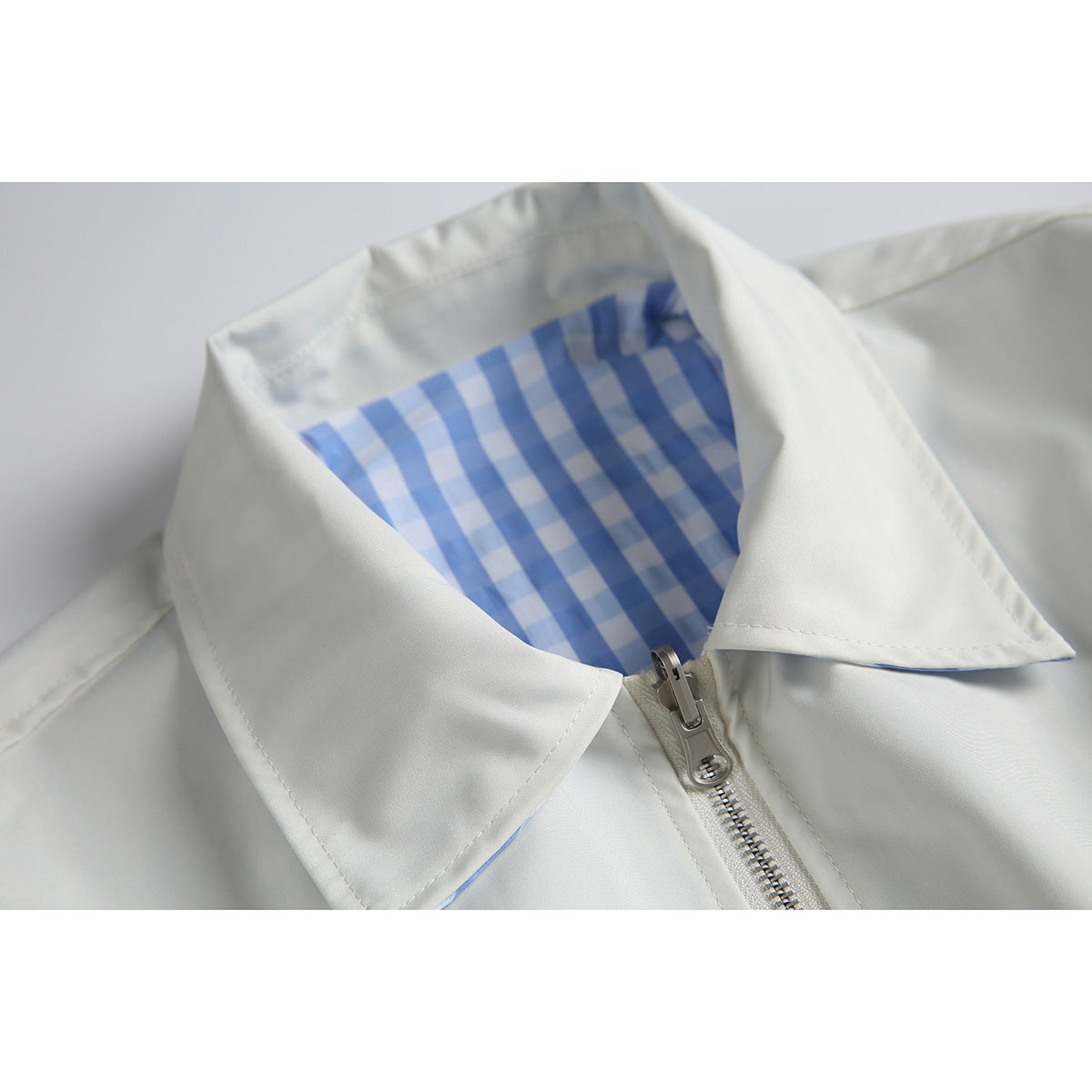 Close-up of a white jacket collar with blue-and-white checked lining and a front zipper.