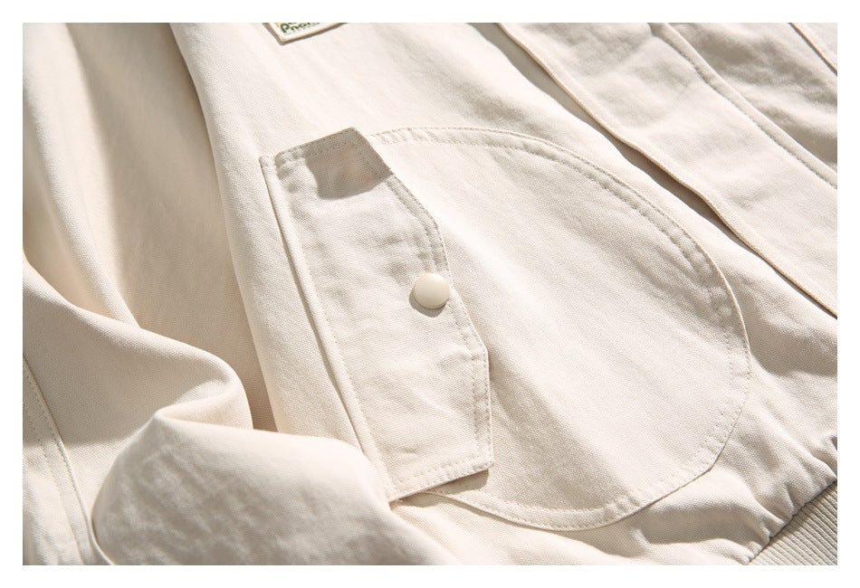 Close-up of an ivory jacket's large rounded front pocket with a snap-fastened flap.