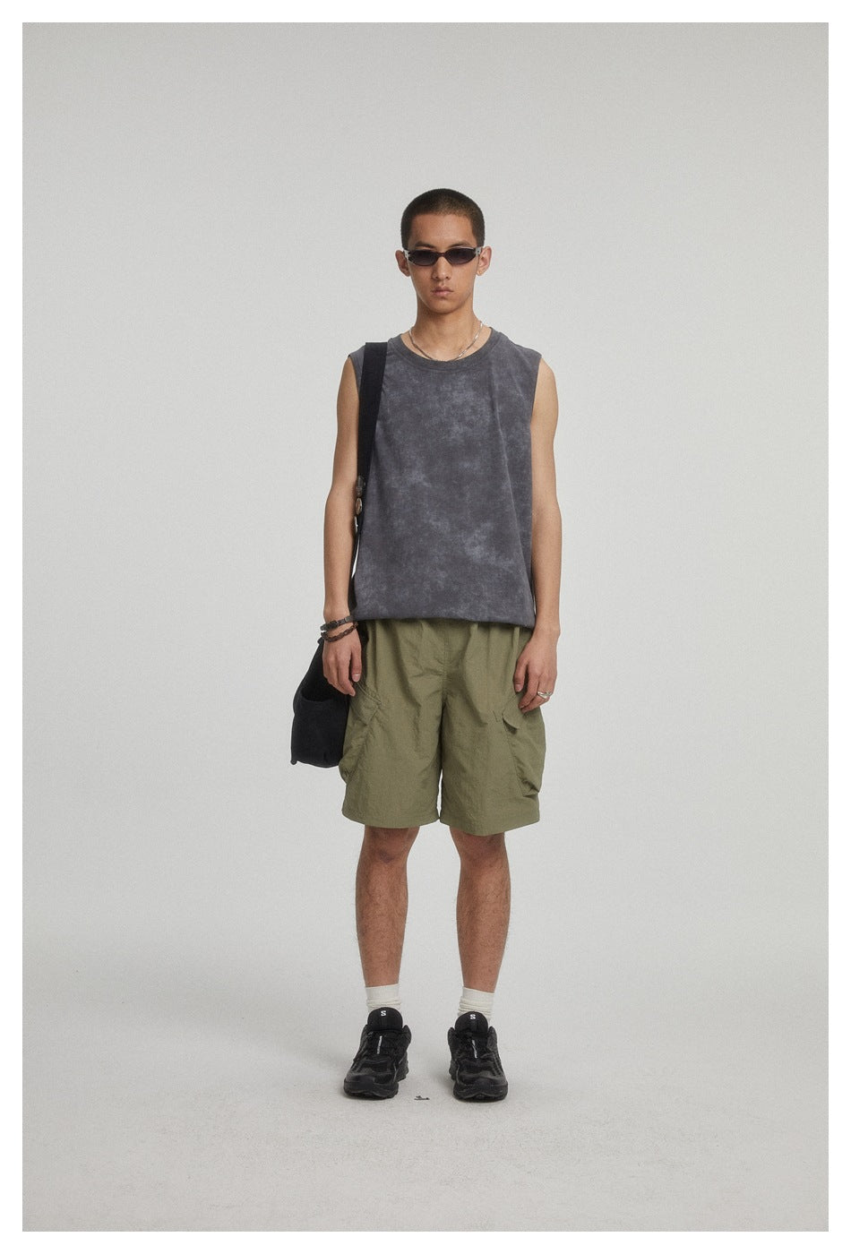 Model wearing army green cargo shorts with a gray sleeveless top, black sneakers and a crossbody bag, full-length view