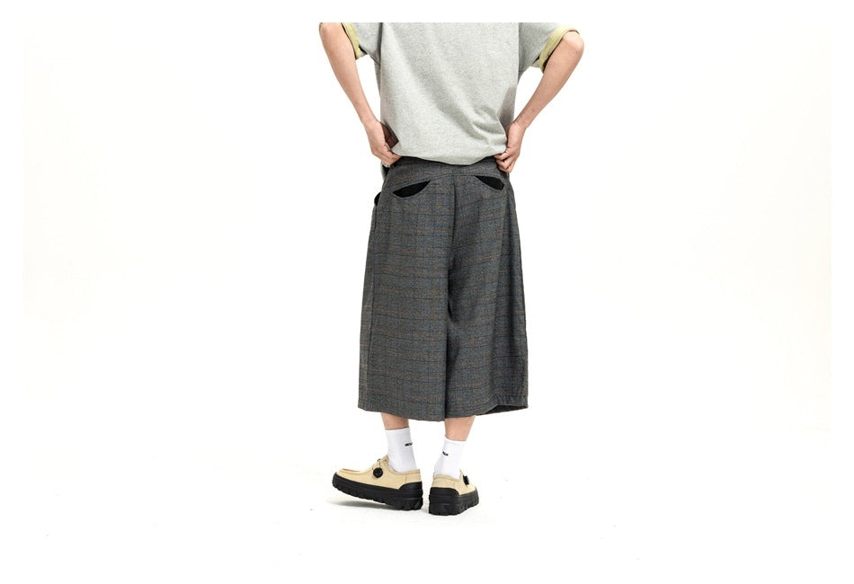 Rear view of a model wearing dark plaid wide-leg shorts with two black-trimmed back pockets.