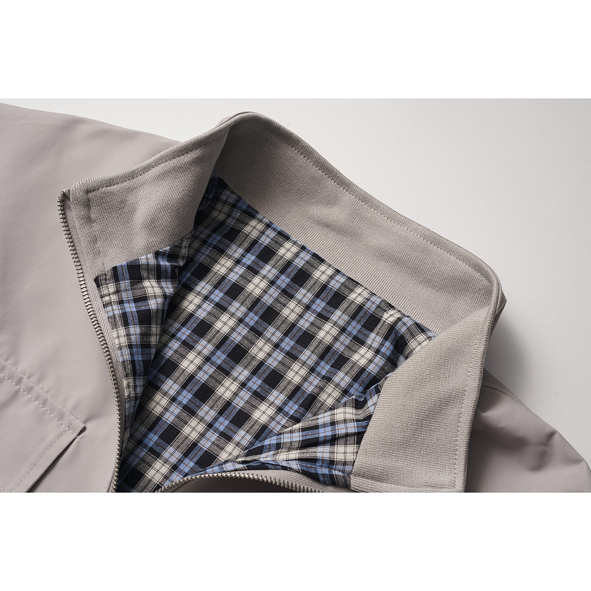 Close-up of a light gray jacket opened to show its blue, black, and cream plaid lining and ribbed collar.