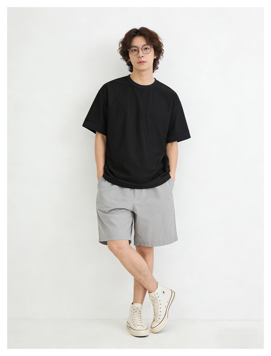 Model with hands in pockets wearing a black oversized short-sleeve t-shirt, gray shorts and cream high-top sneakers