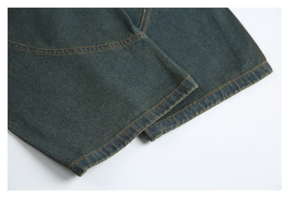 Close-up of dark denim trouser hems and leg seams with orange topstitching.