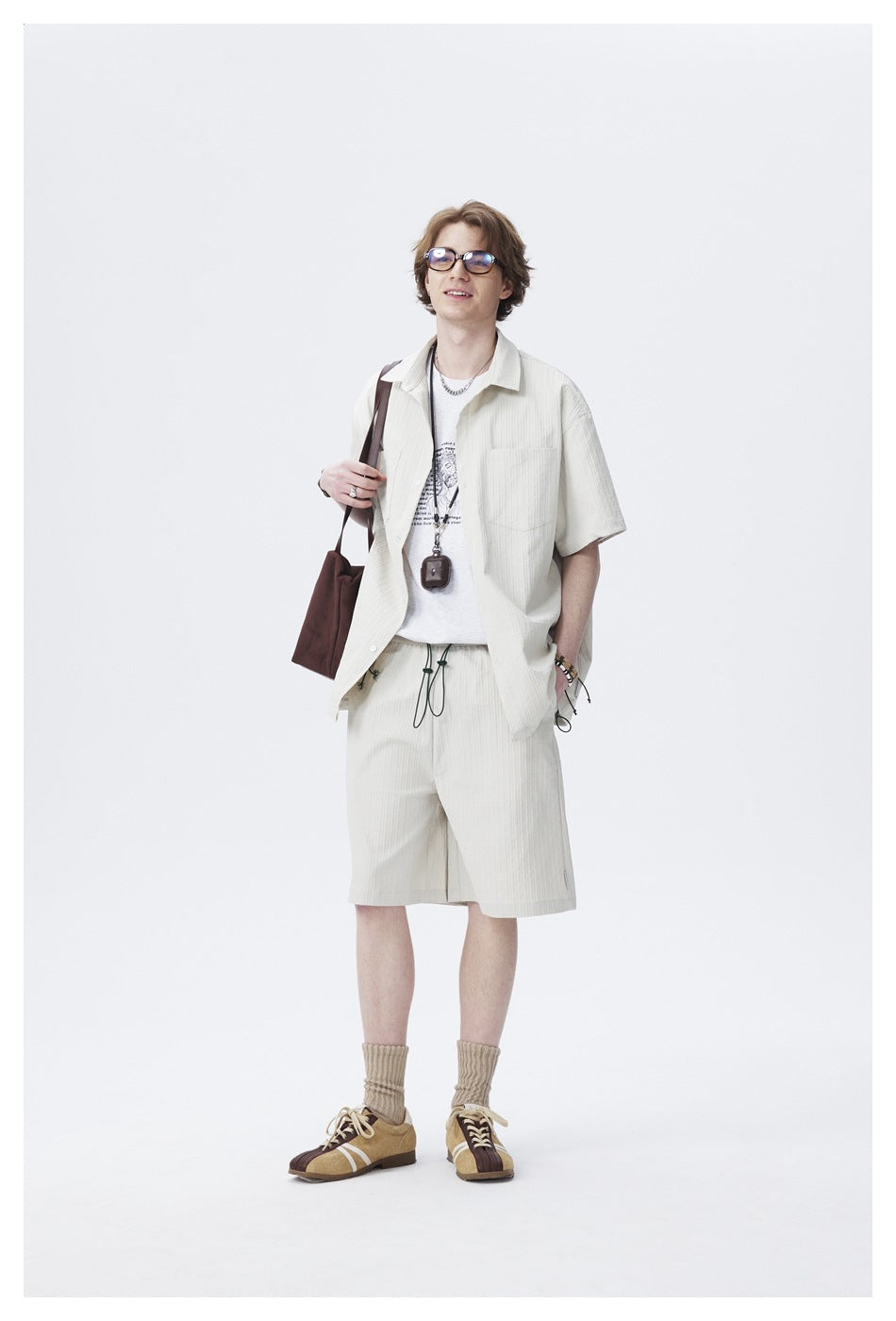 Smiling model in the light short-sleeve shirt worn open over a graphic tee with matching shorts and brown shoulder bag