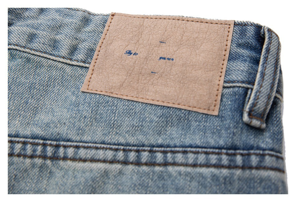 Close-up of a light blue denim waistband, belt loop, and tan leather patch with faint lettering.