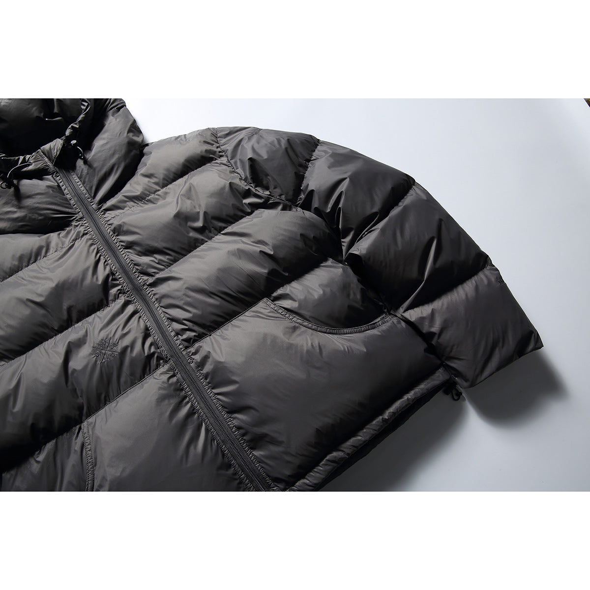 Close-up of a black quilted hooded jacket showing its front zipper, padded panels, and curved pocket.