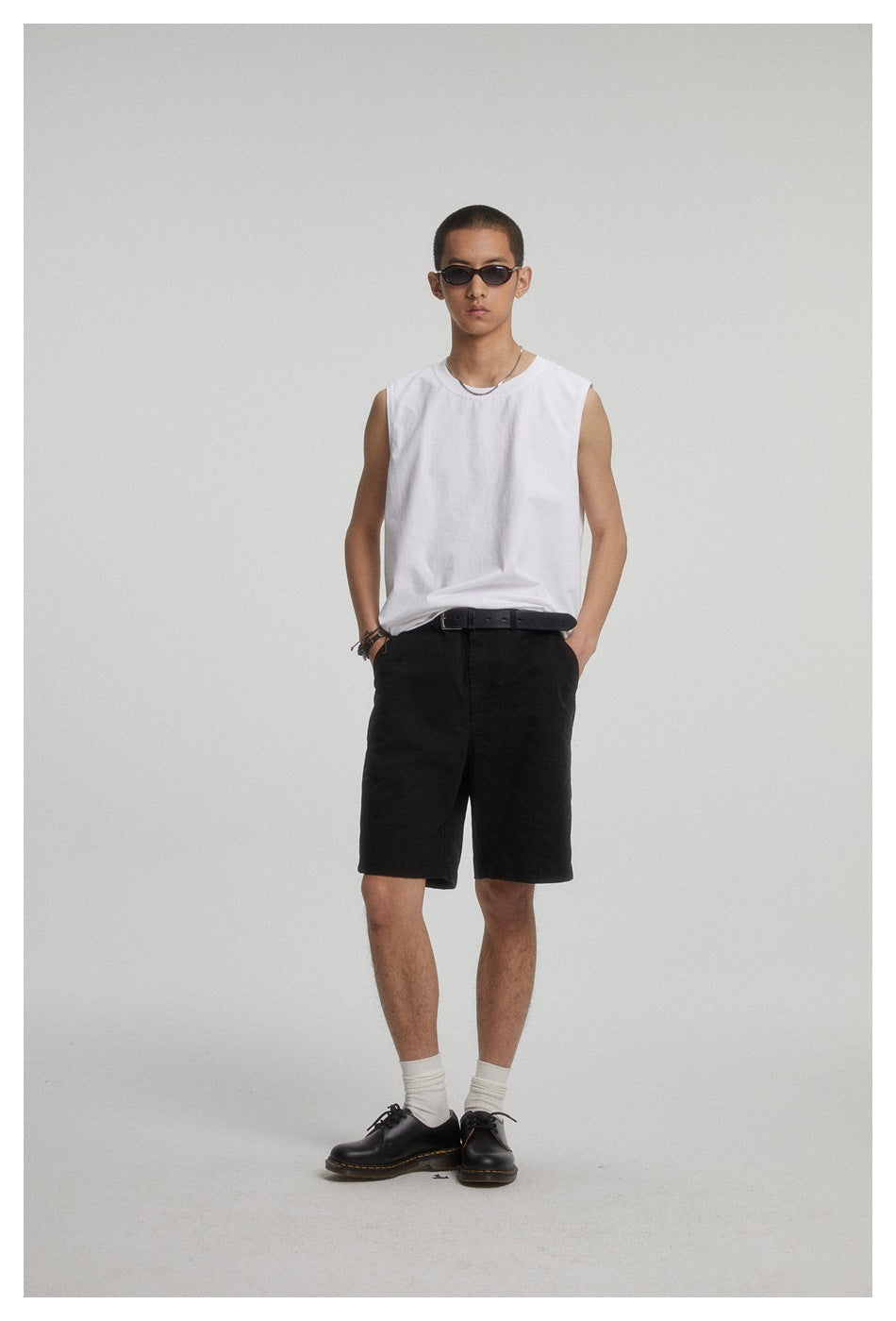 Front view of a model wearing a white sleeveless shirt and black shorts against a plain studio backdrop.