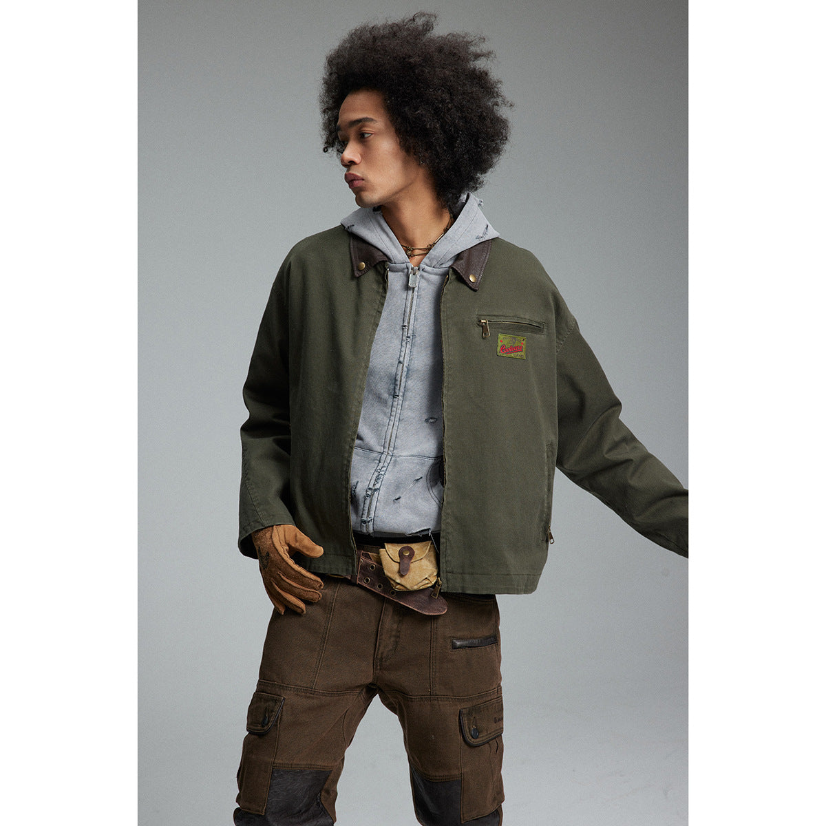 Model wearing an open olive work jacket over a gray hoodie, shown from the front at an angle.