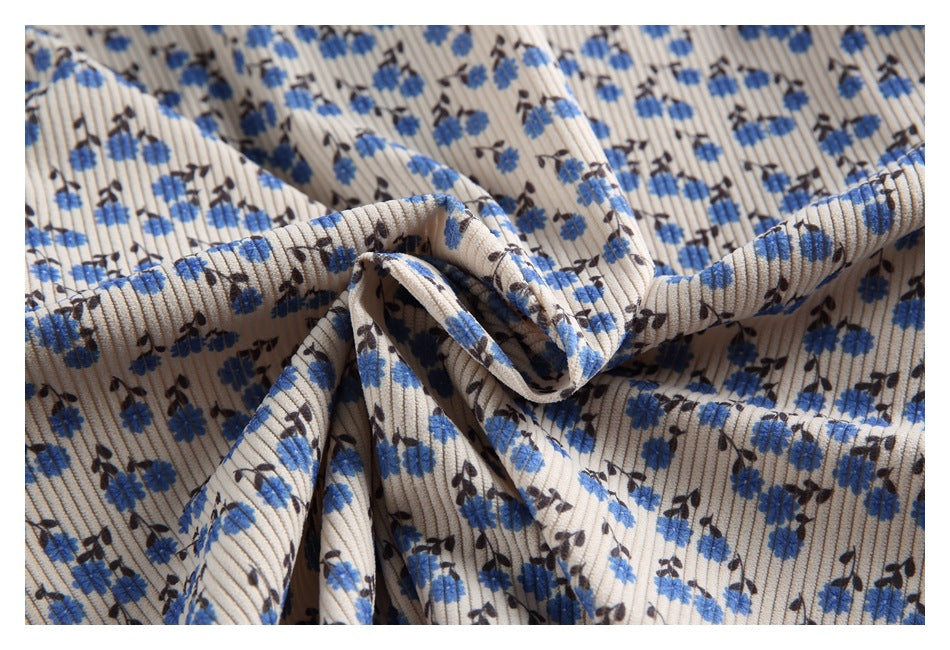 Close-up of beige ribbed fabric with blue and dark flowers, gathered to show its texture and drape.